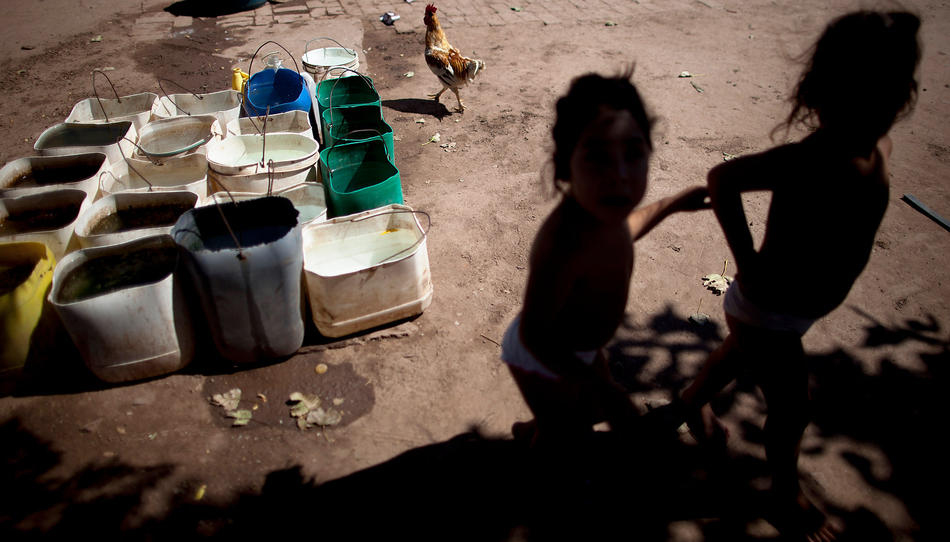 In this March 31, 2013, photo, Erika, left, and her twin sister Macarena, who suffer from chronic respiratory illness, play in their backyard near recycled agrochemical containers filled with water that is used for flushing their toilet, feeding their chickens and washing their clothes, near the town of Avia Terai, in Chaco province, Argentina. The twins’ mother, Claudia Sariski, whose home has no running water, says she doesn’t let her children drink the water from the discarded pesticide containers. (AP Photo/Natacha Pisarenko)