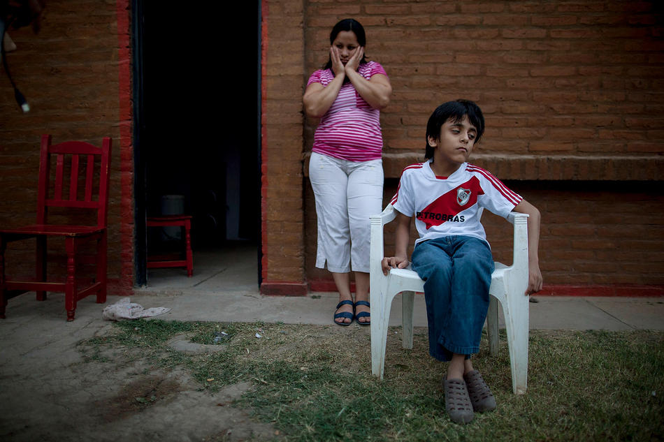 In this April 1, 2013, photo, Silvia Alvarez leans against her red brick home while keeping an eye on her son, Ezequiel Moreno, who was born with hydrocephalus, in Gancedo, in Chaco province, Argentina. Alvarez blames continuous exposure to agrochemical spraying for two miscarriages and her son’s health problems. Chaco provincial birth reports show that congenital defects quadrupled in the decade after genetically modified crops and their related agrochemicals arrived. (AP Photo/Natacha Pisarenko)
