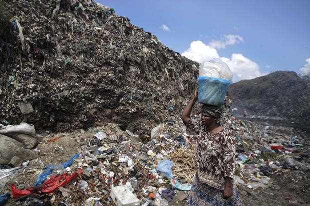 A woman walks down a path between heaps of trash at Dandora dumping site.
